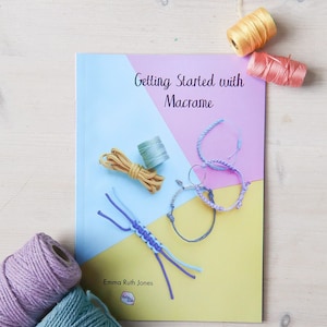 May include: A book titled "Getting Started with Macrame" by Emma Ruth Jones. The book cover features a light blue and pink background with various colours of macrame cord and finished macrame bracelets.