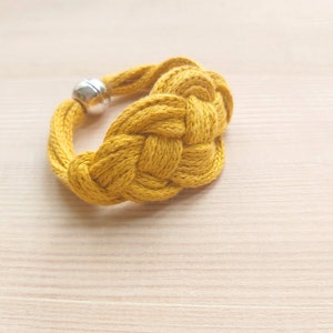 Pu&ograve; includere: Un braccialetto in corda intrecciata giallo con chiusura a perlina argentata.