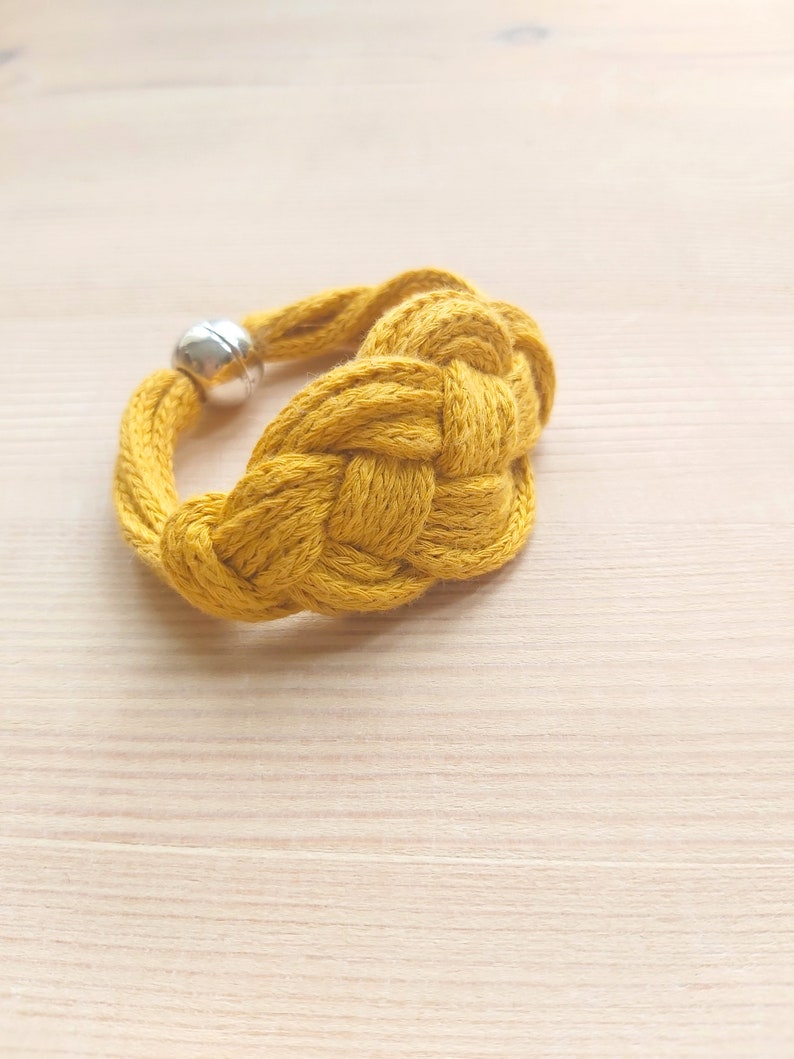 Pu&ograve; includere: Un braccialetto in corda intrecciata giallo con chiusura a perlina argentata.