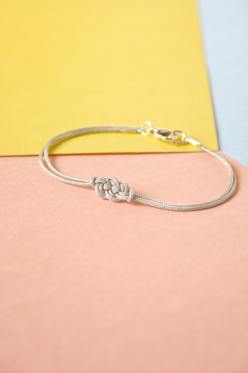 Pu&ograve; includere: Un braccialetto d'argento con un design annodato su uno sfondo rosa chiaro e giallo.