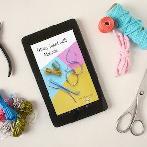 Może przedstawiać: Tablet wyświetlający ebook zatytułowany "Getting Started with Macrame" z kolorowymi bransoletkami z makramą na okładce. Tablet jest otoczony kolorową wł&oacute;czką, nożyczkami i szczypcami.