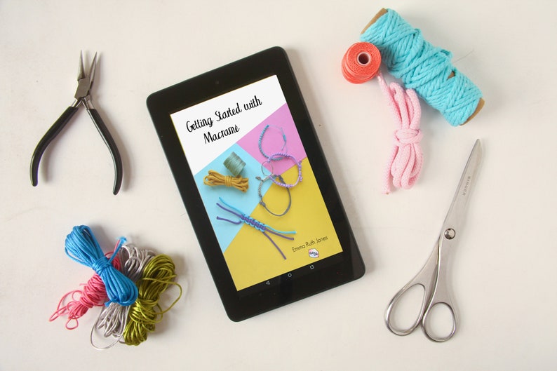 Może przedstawiać: Tablet wyświetlający ebook zatytułowany "Getting Started with Macrame" z kolorowymi bransoletkami z makramą na okładce. Tablet jest otoczony kolorową wł&oacute;czką, nożyczkami i szczypcami.