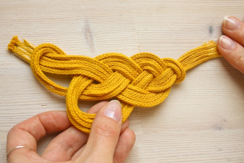 Pu&ograve; includere: Una corda intrecciata gialla annodata a forma di cuore.