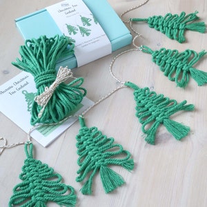 May include: A kit to make a macrame Christmas tree garland. The kit includes green macrame cord, twine, and instructions. The image shows a finished garland with five green macrame Christmas trees.
