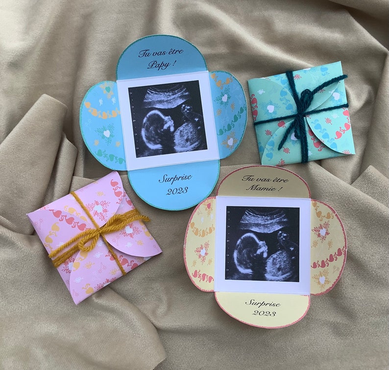 May include: Two yellow, blue, and pink cardstock envelopes with ultrasound images and the text "Tu vas &ecirc;tre Papy!" and "Tu vas &ecirc;tre Mamie!"  The envelopes are tied with twine and ribbon.