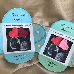 May include: Two blue and green heart-shaped cards with ultrasound images and the text "Tu vas &ecirc;tre Papy! L'amour grandit quand on s&egrave;me! Surprise 2028" and "Tu vas &ecirc;tre Tonton! L'amour grandit quand on s&egrave;me! Surprise 2028".