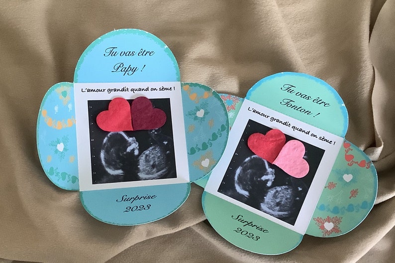 May include: Two blue and green heart-shaped cards with ultrasound images and the text "Tu vas &ecirc;tre Papy! L'amour grandit quand on s&egrave;me! Surprise 2028" and "Tu vas &ecirc;tre Tonton! L'amour grandit quand on s&egrave;me! Surprise 2028".