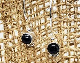 May include: A pair of silver dangle earrings with black gemstone accents. The earrings are on a burlap background.