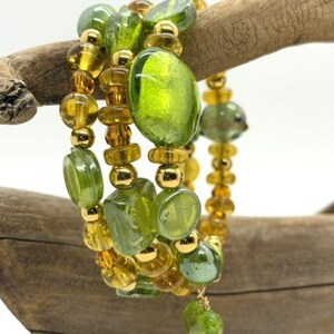 May include: A multi-strand bracelet featuring a mix of translucent lime green glass beads, amber-colored faceted beads, and small metallic gold-tone spacer beads. The design includes various bead shapes, including round, oval, and irregular forms.