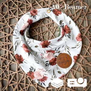 Puede incluir: Babero bandana blanco con un patrón floral en tonos rojos, rosas y verdes. El babero tiene una etiqueta de cuero marrón con el texto "Näheliebe" y un cierre de presión dorado.