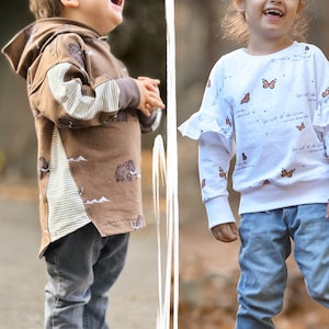 May include: Two children wearing colorful sweatshirts. The child on the left is wearing a brown sweatshirt with a white stripe down the side and a pattern of mammoths. The child on the right is wearing a white sweatshirt with a butterfly pattern and the text "Die Welt ist Wunderbar".