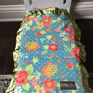 May include: A white doll bed with a blue and white floral patterned blanket with green trim and a Matilda Jane label. The blanket has a satin border.