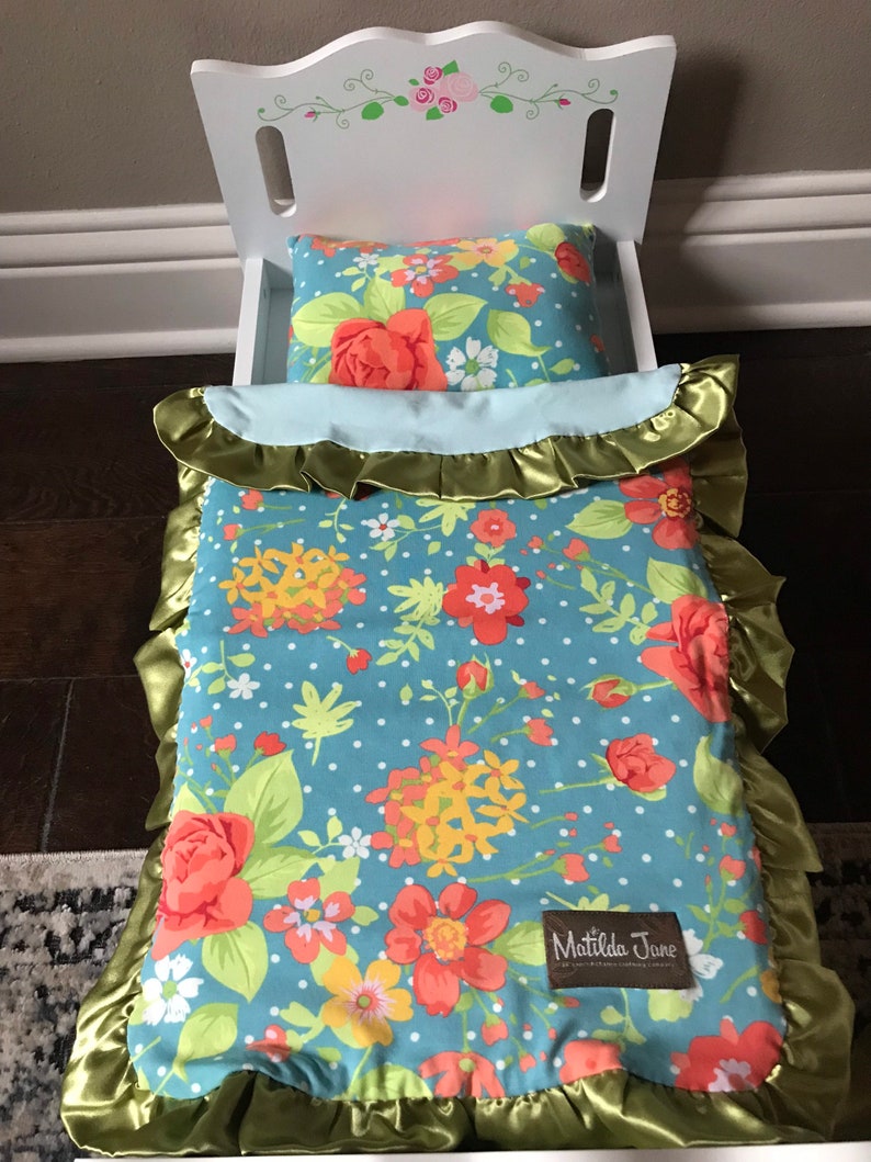 May include: A white doll bed with a floral patterned blue and green comforter and pillow. The comforter has a green ruffled trim and a Matilda Jane label.
