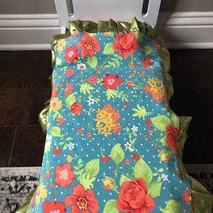 May include: A white doll bed with a floral patterned bedding set. The bedding has a blue background with red, yellow, and green flowers. The bedding has a green ruffled trim.