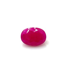 Può includere: Una gemma di rubino sfaccettata a forma ovale. La gemma è di un colore rosso intenso e vibrante ed è posta su uno sfondo bianco. Le sfaccettature del rubino catturano la luce, creando un effetto scintillante.