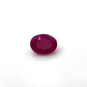 Op de afbeelding: Een gefacetteerde, ovaalvormige robijn edelsteen. De edelsteen heeft een diepe, verzadigde rode kleur, met een gepolijst oppervlak dat licht reflecteert. De robijn is geplaatst tegen een witte achtergrond, wat de kleur en helderheid benadrukt.