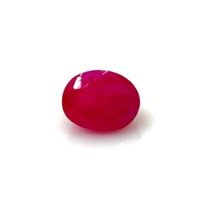 Pode incluir: Uma gema polida, de forma oval, em um tom magenta profundo. A gema está sobre um fundo branco limpo, destacando sua superfície lisa e reflexiva. Esta gema pode ser usada em joias.