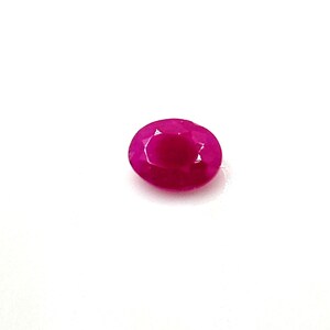 Pode incluir: Uma gema de rubi com corte oval. A gema é de um vermelho profundo e saturado, com facetas que capturam a luz. O rubi é apresentado sobre um fundo branco liso, realçando sua cor e clareza.