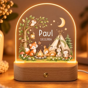 Puede incluir: Una luz nocturna de acrílico arqueada con base de madera que presenta una escena de bosque con un zorro, ciervo, conejo, erizo, búho, fogata y tienda de campaña. El texto "Paul" y "13.11.2026" está impreso en el centro con luz cálida.