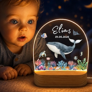 May include: An arched acrylic night light with a wooden base featuring a printed whale, sea turtle, and colorful coral reef. The text Elias and 19.06.2026 are printed in white. The light illuminates the design with a warm glow from the base.