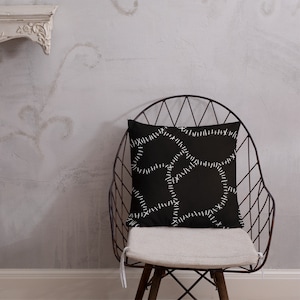 May include: Black throw pillow with white stitching in a stitched pattern. The pillow is sitting on a black metal chair with a white cushion.