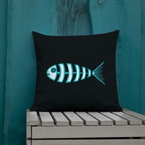 May include: A black throw pillow with a turquoise blue fish skeleton design. The fish has a single eye and a cross for a pupil.