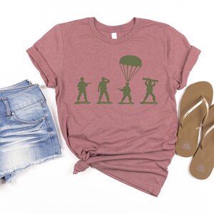 a casual outfit consisting of a pink t-shirt with a graphic of soldiers, denim shorts, and brown flip-flops.