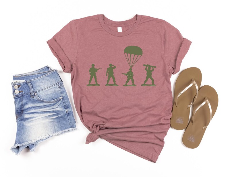 a casual outfit consisting of a pink t-shirt with a graphic of soldiers, denim shorts, and brown flip-flops.