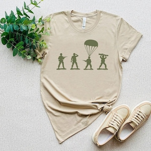 a beige t-shirt with a graphic design depicting a group of soldiers, along with a pair of sneakers and a plant.
