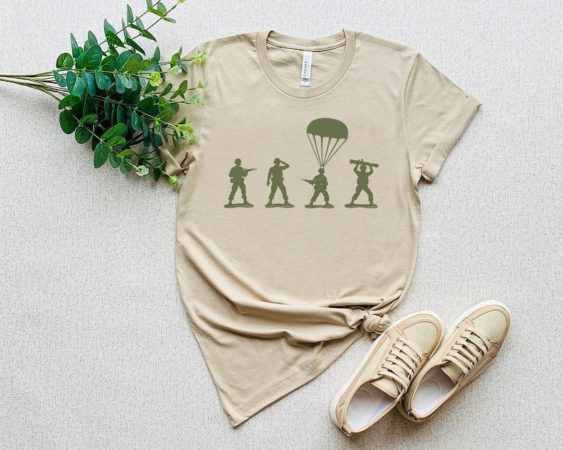 a beige t-shirt with a graphic design depicting a group of soldiers, along with a pair of sneakers and a plant.