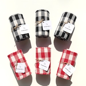 May include: Six rolled fabric pieces in black and white, and red and white checkered patterns. Each roll is tied with twine and has a tag that reads "burlapcrafts.co". The fabric is arranged on a white surface.
