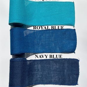 May include: Three rolls of burlap ribbon in turquoise, royal blue, and navy blue. The ribbon is tightly woven and has a textured appearance. The colors are vibrant and saturated, with the names of the colors printed above each roll.