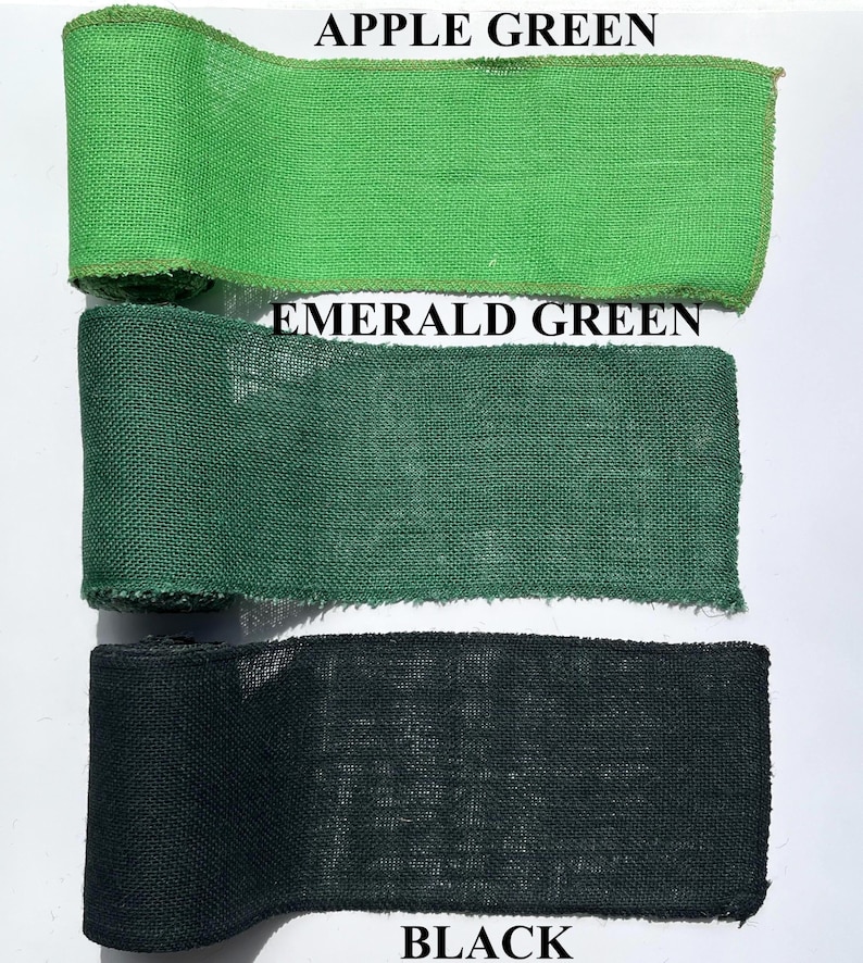 May include: Three rolls of burlap ribbon in shades of green and black. The top roll is apple green, the middle is emerald green, and the bottom is black. The text "APPLE GREEN", "EMERALD GREEN", and "BLACK" are printed above each ribbon.