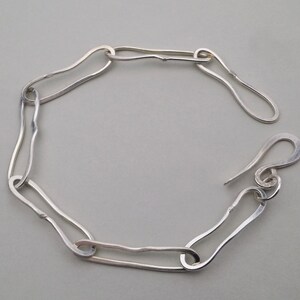 May include: A silver bracelet with a unique, organic design. The bracelet is made of interconnected, wavy links that create a flowing, modern look.