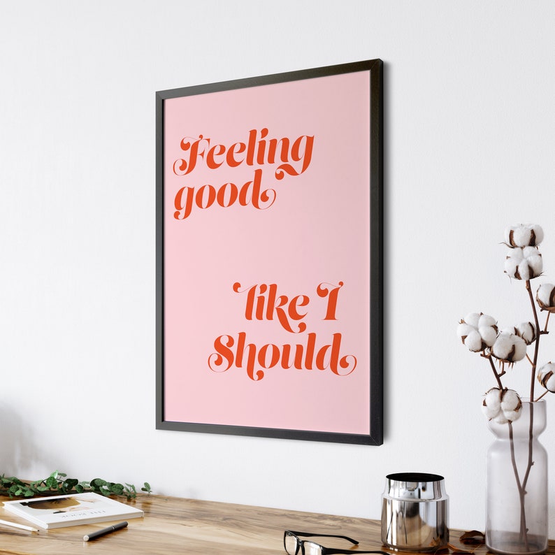 Puede incluir: Una impresi&oacute;n enmarcada rosa con el texto "Feeling good like I should" en fuente cursiva roja.