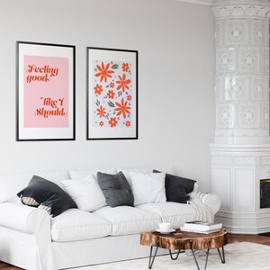 Puede incluir: Dos impresiones enmarcadas en una pared blanca sobre un sof&aacute; blanco. La impresi&oacute;n de la izquierda tiene un fondo rosa con el texto "Feeling good, like I should." La impresi&oacute;n de la derecha tiene un fondo blanco con un patr&oacute;n de flores naranjas.