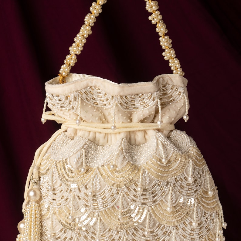 May include: A white beaded drawstring bag with a gold chain handle. The bag is decorated with pearl-like beads and sequins in a scalloped pattern.