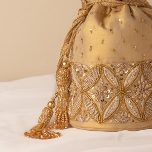 May include: A gold drawstring bag with a beaded tassel. The bag is decorated with gold and silver sequins and beads in a floral pattern.