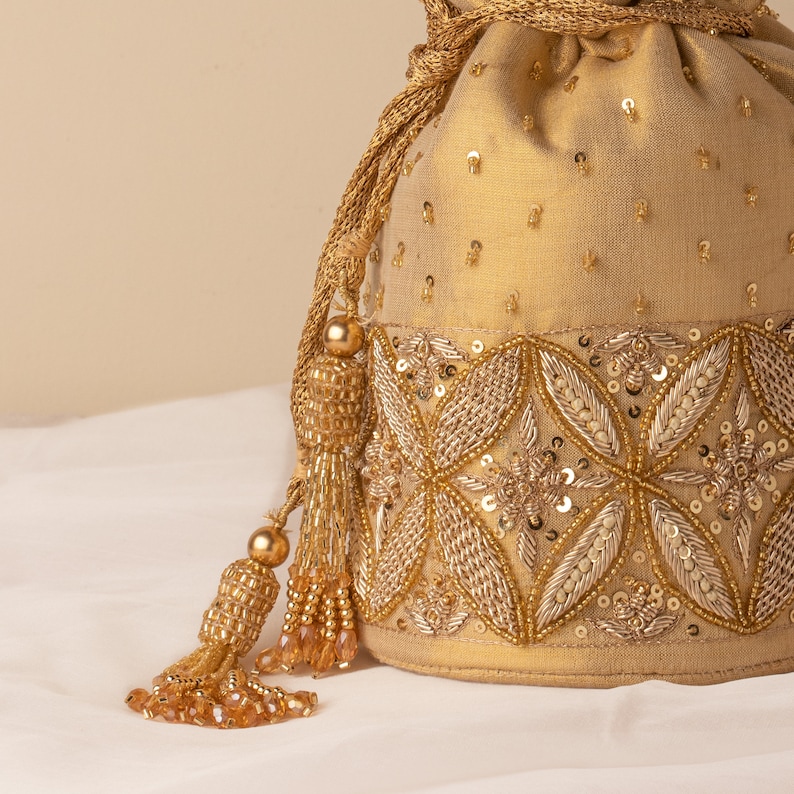 May include: A gold drawstring bag with a beaded tassel. The bag is decorated with gold and silver sequins and beads in a floral pattern.