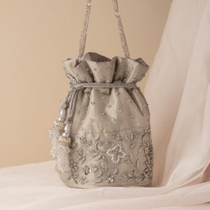 Può includere: Una borsa a cordoncino argentata con una tracolla perlata e ricami floreali. La borsa è decorata con paillettes e perle.
