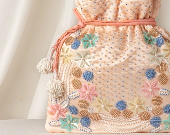Puede incluir: Una bolsa de cordón de color melocotón con un diseño floral. La bolsa está decorada con cuentas y lentejuelas de colores, y tiene un borla en el lateral.