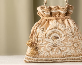 May include: A cream-coloured drawstring bag with a beaded floral design and gold accents. The bag has a beaded handle and a tassel.