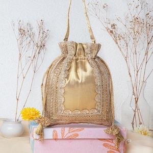 May include: A gold drawstring bag with a beaded trim and a tassel. The bag is made of satin and has a delicate, feminine design.