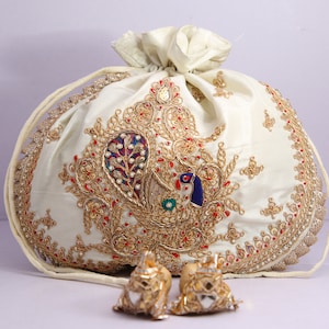 May include: A white silk pouch with gold, red and blue embroidery depicting a peacock. The pouch has a drawstring closure and is decorated with pearls and sequins.