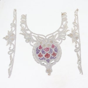 May include: A silver and white beaded neckline with a colorful floral design in the center. The neckline is separated into three pieces, with two long pieces for the sides and a shorter piece for the front.