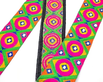 Op de afbeelding: Een kleurrijke geborduurde bies met een geometrisch patroon van cirkels en vierkanten. De bies is roze, groen, blauw, geel en oranje van kleur en is versierd met kleine, gespiegelde vierkanten.