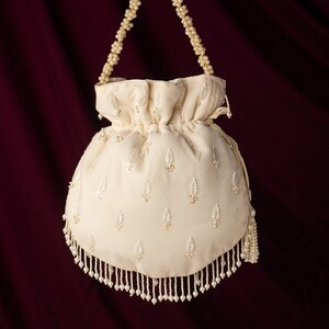 May include: A white drawstring bag with a beaded handle and fringe. The bag is decorated with a pattern of small white beads.