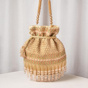 May include: Gold-colored beaded drawstring bag with a textured pattern. The bag features red, green, and pink accents, a gold rope drawstring, and beaded fringe. The handles are made of gold beads.