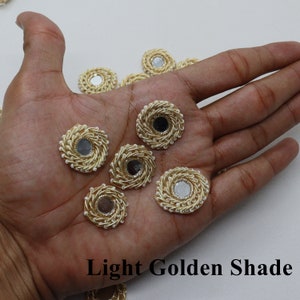 Op de afbeelding: Een close-up van acht ronde, goudkleurige, decoratieve versieringen met een spiegel in het midden. De versieringen zijn omgeven door een witte parelrand. De tekst "Light Golden Shade" is zichtbaar onderaan de afbeelding.