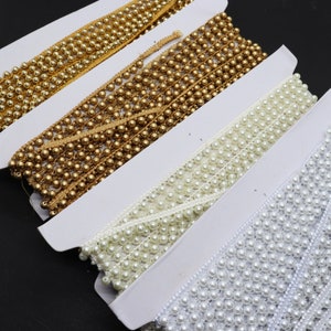 May include: Four spools of beaded trim, two gold, one white, and one ivory. The trim is made of small, round beads sewn onto a thin ribbon.